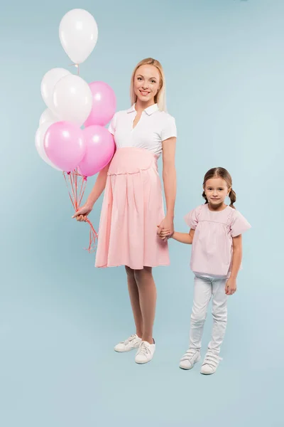 Longitud completa de la mujer embarazada feliz sosteniendo globos cerca de la hija en azul - foto de stock