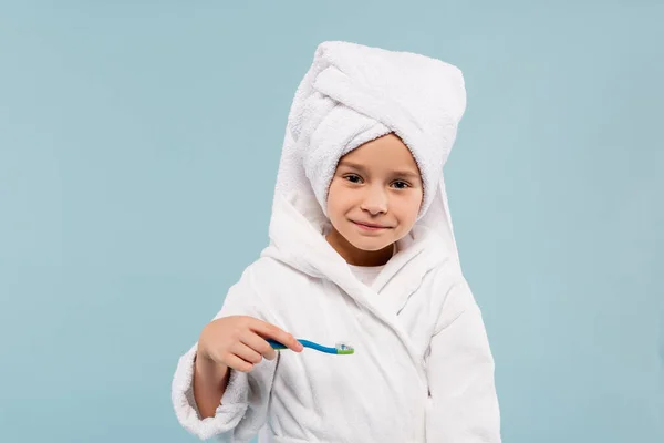 Счастливый ребенок в халате и полотенце на голове держа зубную щетку с зубной пастой изолированы на синий — стоковое фото
