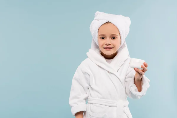 Lächelndes Kind im Bademantel und Handtuch auf dem Kopf Aufbewahrungsbehälter mit Kosmetikprodukt isoliert auf blau — Stockfoto