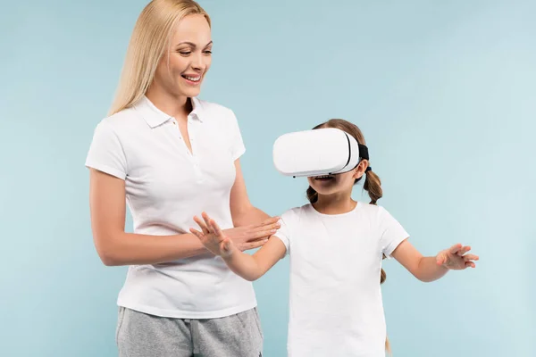 Веселая мать улыбается рядом с дочерью в VR гарнитуре изолированы на синий — стоковое фото