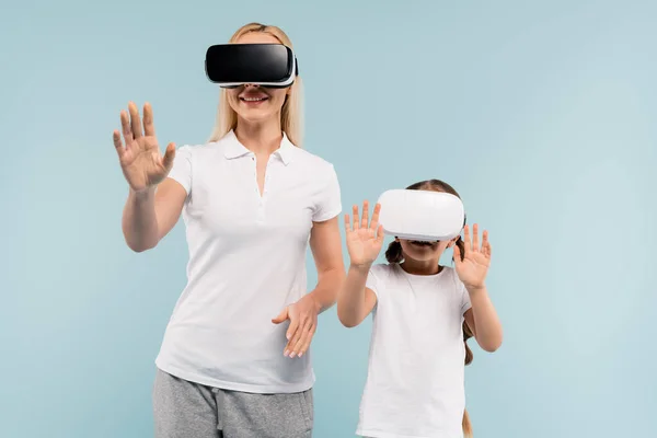 Mãe alegre e criança em fones de ouvido vr gesticulando isolado em azul — Fotografia de Stock