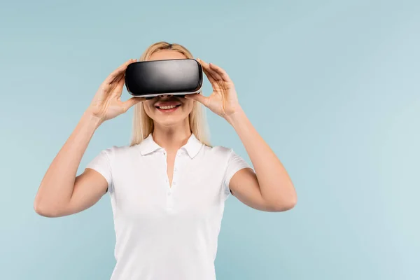 Fröhliche blonde Frau stellt vr Headset isoliert auf blau ein — Stockfoto