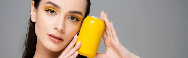 Брюнетка молодая женщина держит желтую банку с безалкогольным напитком изолированы на сером, баннер — стоковое фото
