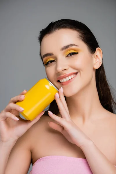 Счастливая молодая женщина держит желтую банку с безалкогольным напитком изолированы на серый — стоковое фото