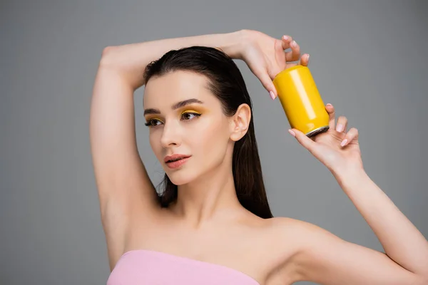 Брюнетка молодая женщина с голыми плечами, держащая желтую банку с безалкогольным напитком, изолированным на сером — стоковое фото