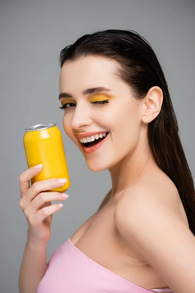 Eccitato giovane donna in possesso di lattina gialla con soft drink e occhio ammiccante isolato su grigio — Foto stock