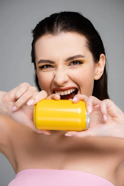 Молодая женщина кричит, держа желтую банку с безалкогольным напитком, изолированным на сером — стоковое фото