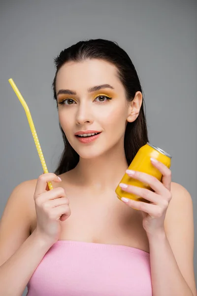 Счастливая молодая женщина держит желтую банку с безалкогольным напитком и соломой, изолированной на сером — стоковое фото