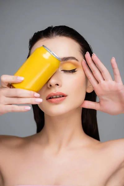 Брюнетка молодая женщина с закрытыми глазами, держащая желтую банку с безалкогольным напитком, изолированным на сером — стоковое фото