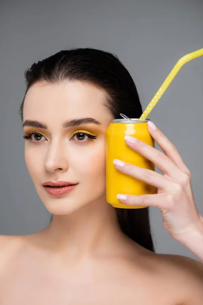 Brunetta giovane donna in possesso di lattina gialla con bibita analcolica con paglia vicino al viso isolato su grigio — Foto stock