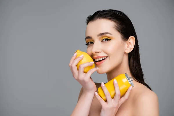 Щаслива молода жінка тримає жовту банку з безалкогольним напоєм і стиглим лимоном ізольовано на сірому — стокове фото