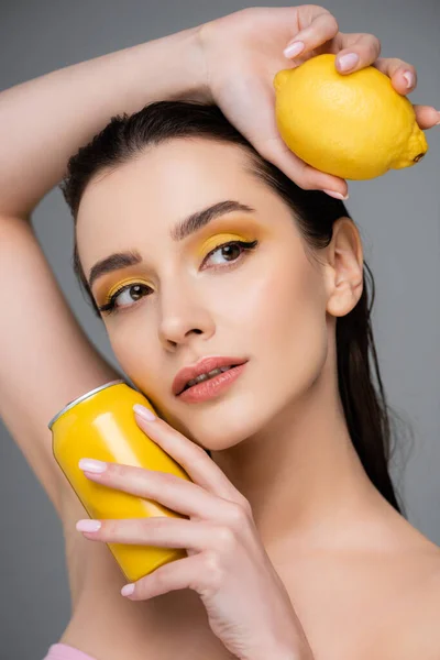 Junge Frau mit gelber Dose mit Softdrink und reifer Zitrone isoliert auf grau — Stockfoto