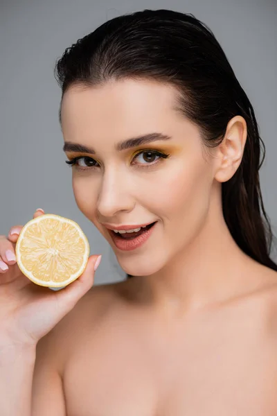 Amazed woman with bare shoulders holding yellow lemon half isolated on grey — Stock Photo