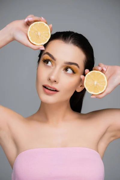 Young woman with bare shoulders holding yellow lemon halves isolated on grey — Stock Photo