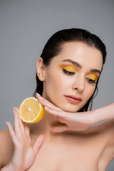 Young woman with bare shoulders holding half of ripe lemon and looking away isolated on grey — Stock Photo