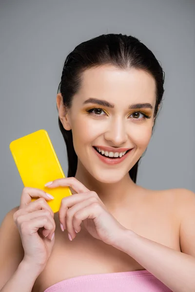 Весела жінка тримає жовте дзеркало ізольовано на сірому — стокове фото