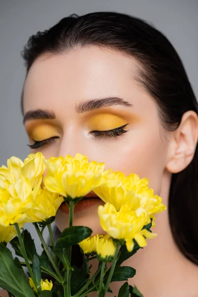 Jovem com sombras amarelas e olhos fechados cobrindo rosto com flores isoladas em cinza — Fotografia de Stock