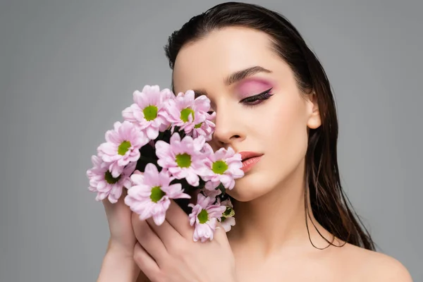 Brunette jeune femme avec des ombres à paupières roses tenant des fleurs isolées sur gris — Photo de stock