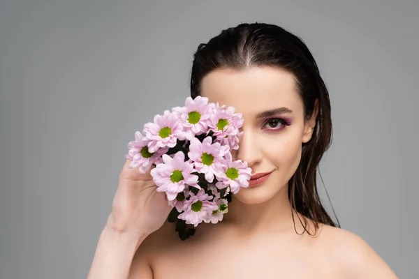 Jeune femme aux ombres à paupières roses couvrant le visage de fleurs isolées sur gris — Photo de stock