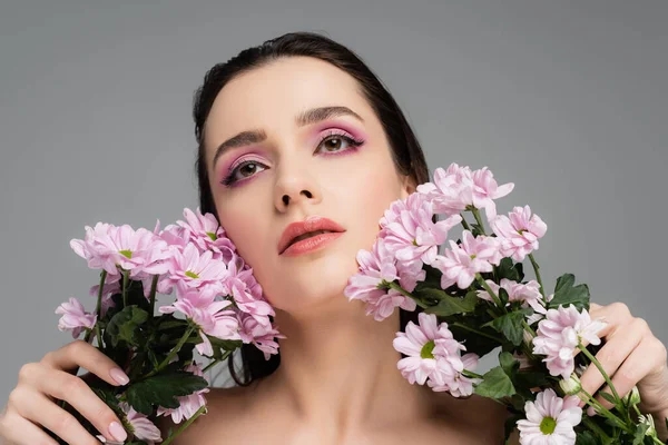 Jovem mulher com sombras de olhos rosa segurando flores e olhando para cima isolado em cinza — Fotografia de Stock