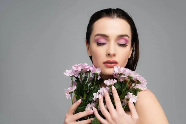 Young woman with pink eye shadows holding bouquet of flowers isolated on grey — Stock Photo