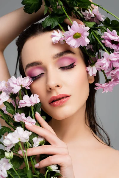 Jovem com olhos fechados e sombras de olhos cor-de-rosa segurando flores isoladas em cinza — Fotografia de Stock
