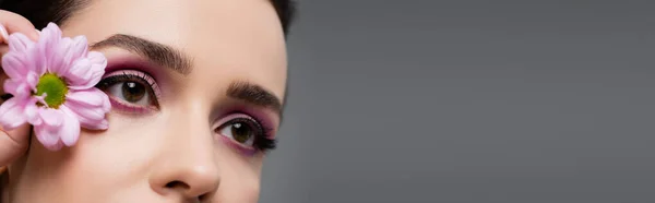 Visão parcial de mulher sensual com sombras de olho rosa segurando flor isolada em cinza, banner — Fotografia de Stock