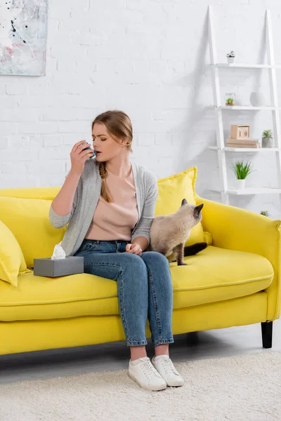 Young woman with allergy using inhaler near napkin and siamese cat — Stock Photo