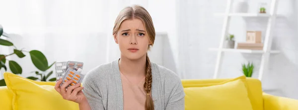 Грустная женщина с аллергией, держащая волдыри с таблетками и глядя в камеру дома, баннер — стоковое фото