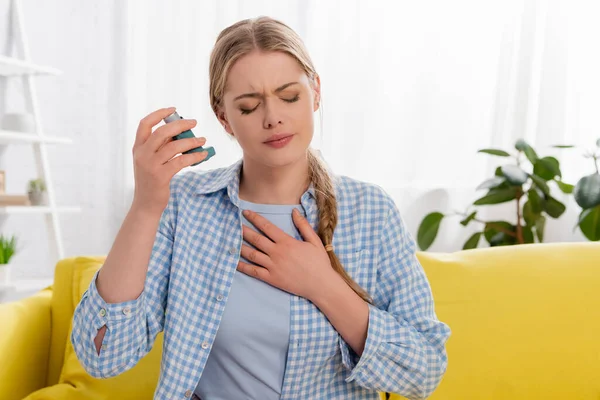 Sick woman with asthma holding inhaler on couch — Stock Photo