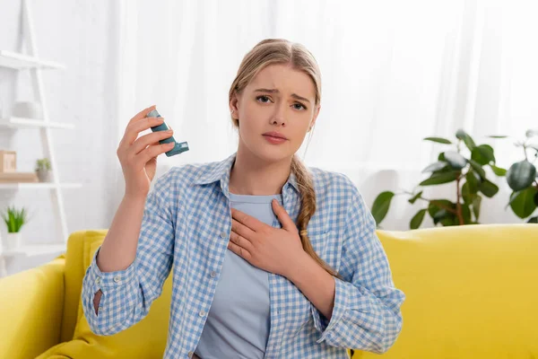 Displeased woman with allergy reaction holding inhaler on couch — Stock Photo