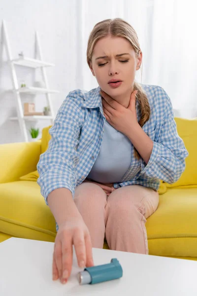 Mujer enferma con alergia tirando de la mano al inhalador en primer plano borroso - foto de stock