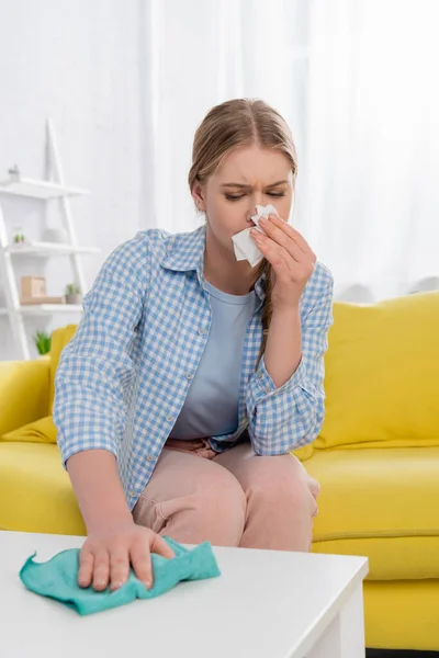 Mujer con alergia teniendo snuffle durante la limpieza de la mesa en primer plano borrosa - foto de stock