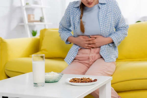 Cropped view of nuts, milk and cottage cheese near woman with allergy on blurred background - foto de stock