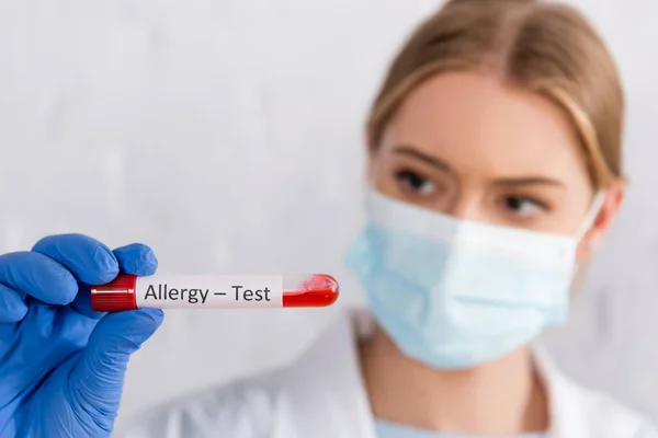 Tube with allergy test lettering in hand of doctor in medical mask on blurred background — Stock Photo