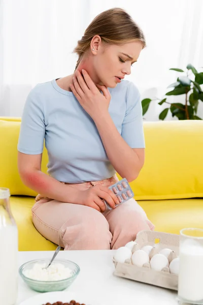 Junge Frau leidet an Allergie, während sie Tabletten in der Nähe von Lebensmitteln hält — Stockfoto