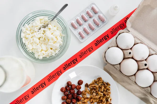 Вид красной ленты с аллергическими надписями возле таблеток, глазных капель и продуктов питания — стоковое фото