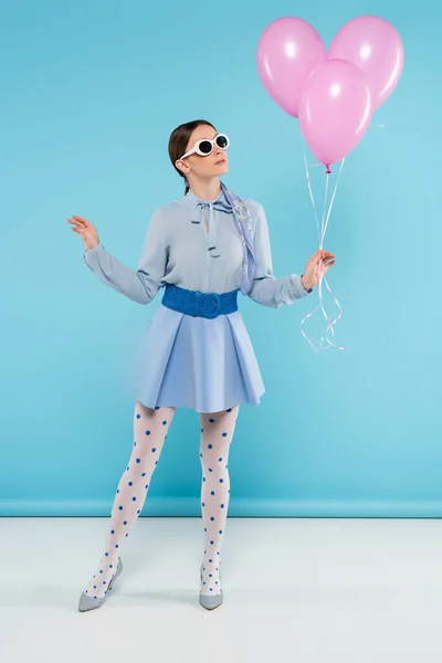 Extravagant woman in dotted tights and sunglasses posing with pink balloons on blue background — Stock Photo