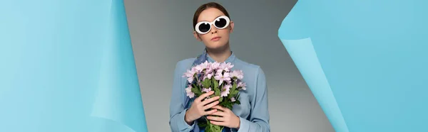 Glamour-Frau mit Sonnenbrille, rosa Blumen in der Nähe von Loch in blauem Papier auf grauem Hintergrund, Banner — Stockfoto