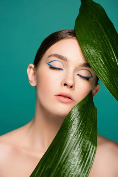 Портрет жінки з блакитною підводкою на закритих очах біля блискучих листя ізольовані на зеленому — стокове фото
