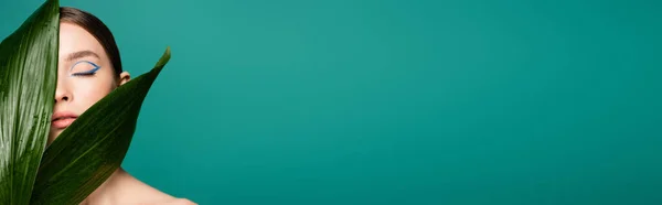 Mujer sensual con delineador de ojos azul cerca de hojas brillantes aisladas en verde, bandera - foto de stock