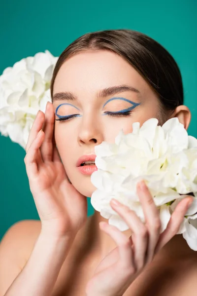 Charming woman with blue eyeliner on closed eyes posing with white peonies isolated on green — Stock Photo