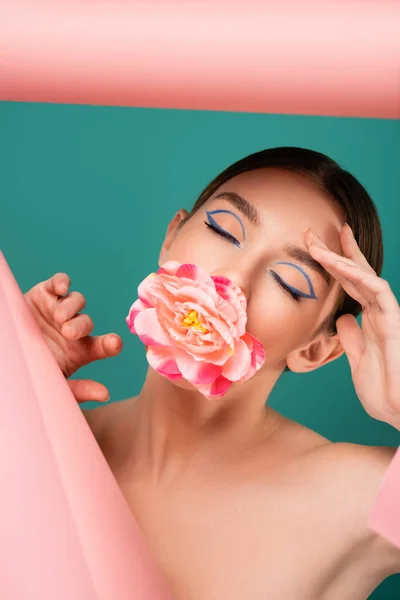 Charming woman with closed eyes and peony in mouth near hole in pink paper isolated on green — Stock Photo