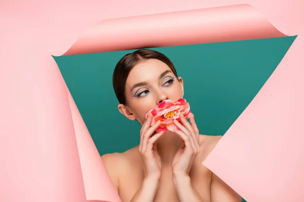 Pretty woman with peony near mouth looking out hole in pink paper isolated on green — Stock Photo