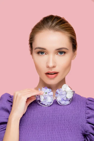 Bonita mujer en blusa lila, sosteniendo anteojos con flores aisladas en rosa - foto de stock