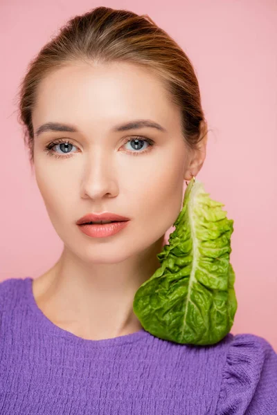 Encantadora mujer con maquillaje natural y pendiente de lechuga fresca aislada en rosa - foto de stock