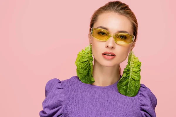 Charmante femme en lunettes de couleur et boucle d'oreille de laitue fraîche regardant la caméra isolée sur rose — Photo de stock