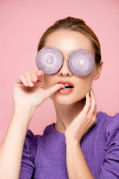 Femme sensuelle dans des lunettes avec des rondelles d'oignon violet, pouce mordant isolé sur rose, concept de surréalisme — Photo de stock