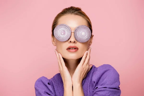 Jeune femme dans des lunettes avec des rondelles d'oignon, posant avec les mains près du visage isolé sur rose, concept de surréalisme — Photo de stock