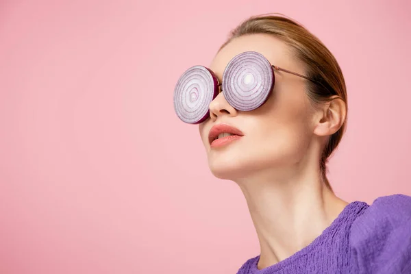Young woman posing in eyeglasses with purple onion rings isolated on pink, surrealism concept — Stock Photo